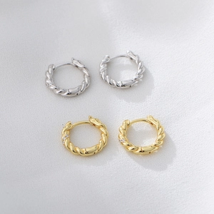 Dettaglio macro di orecchini a cerchio intrecciati in oro e argento con zirconi incastonati