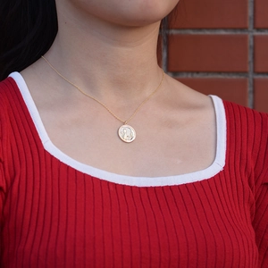 Detail of a golden round embossed pendant necklace with fine chain on a model wearing red