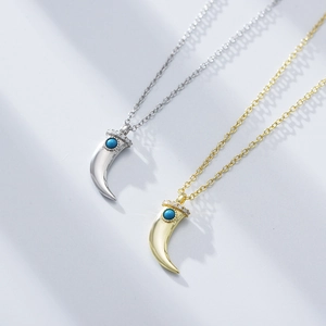 Silver and gold crescent necklaces with turquoise stones and zircons on a gray background