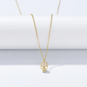 Close-up of a gold skull pendant necklace with micro-paved white zircons on a white pedestal