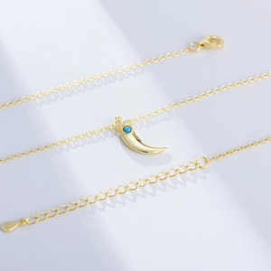 Macro view of gold horn necklace with turquoise stone, pavé zircons and lobster clasp