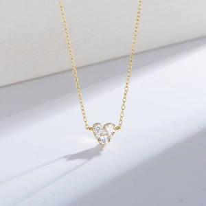 Gros plan du collier pendentif coeur doré avec trois zircons sur socle blanc épuré