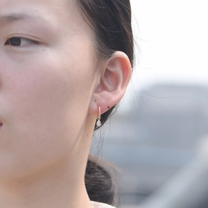 Detailed view of model wearing gold C-shaped earrings with pear-cut zircon pendants