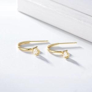 Detail of minimalist J-shaped gold-plated silver earrings with round zircon studs