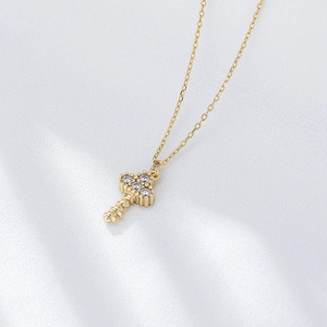 Detailed view of a gold key pendant with four inset crystals on a soft silk background