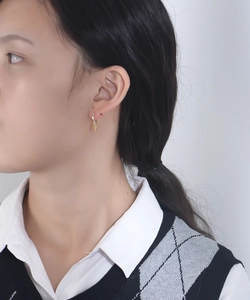 Detailed close-up of a golden teddy bear pendant earring worn by a model in soft lighting