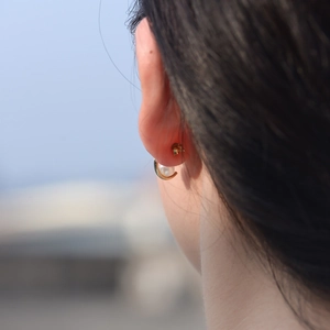 Macro view of gold C-shaped sterling silver hoop earring with pearl on female model