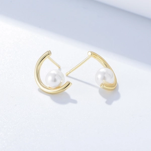 Detailed close-up of golden C-shaped sterling silver earrings with round white pearls