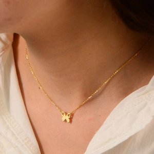 Close-up of minimalist gold butterfly pendant necklace on a woman's neck