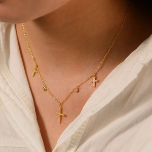 Detail view of gold cross necklace with zircon pendants on model with white shirt
