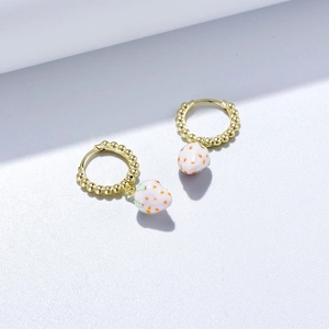 Détail de boucles d'oreilles fraise en argent s925 avec texture perlée dorée et émail blanc