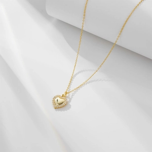 Gros plan d'un pendentif cœur doré serti de zircons sur un support blanc