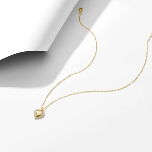 Détail du collier pendentif cœur doré orné de zircons scintillants sur fond blanc minimaliste