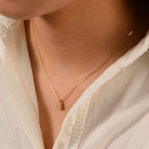 Close-up of gold pear-shaped pendant with pavé cubic zirconia worn by model