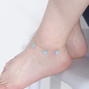 Gold anklet with three light blue flower pendants and zircons shown on ankle