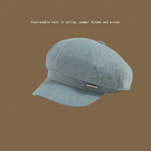 Close-up of light blue washed denim octagonal newsboy hat with a metal logo plate