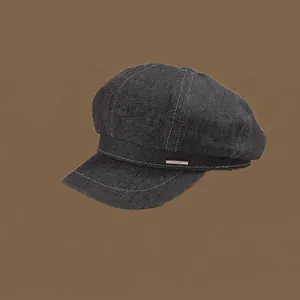 Detail of a black denim newsboy cap featuring white contrast stitching and a metal emblem