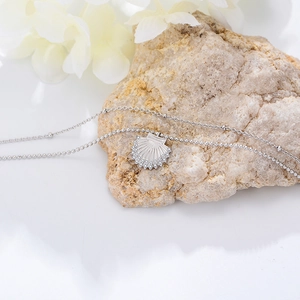 Detailed macro of a silver layered seashell necklace with sparkling zircons on white stone