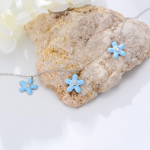 Detail of silver anklet with blue enamel flower charms over a natural stone