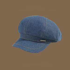 Close-up of deep blue denim octagonal hat with yellow stitching and metal brand tag