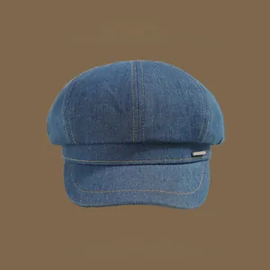 Detailed close-up showing the twill texture and metal trim of a blue denim newsboy cap
