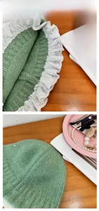 Detail of green knit bucket hat with white lace trim and soft wool texture on wooden surface