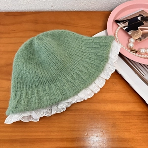 Pale green knitted bucket hat with white lace trim shown on a wooden background