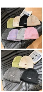 Collection of various colored knitted beanies with small leather tags on textured surface