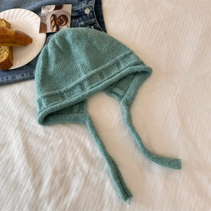 Cozy turquoise knit earflap hat with tie strings on a decorative rustic background