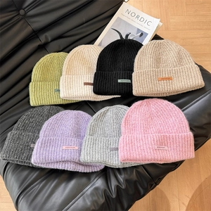 Multiple colorful rib-knit beanies with letter patches on a stylish black leather bench