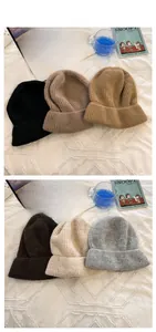 Flat lay of ribbed knit beanies in assorted neutral colors on a white textured blanket