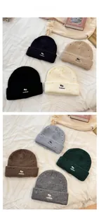 Close-up of thick knit beanies with embroidered fox motif and decorative ripped details