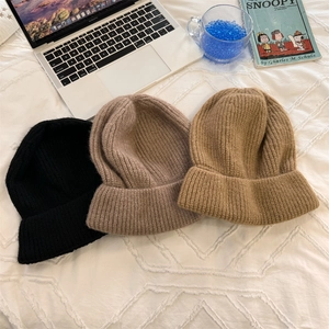 Three oversized knitted beanies in black, coffee, and light brown on a white bed sheet