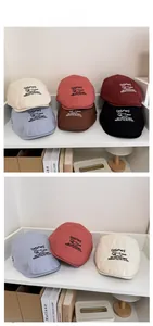 Detail display showing six colors of embroidered cotton flat caps on a bookshelf