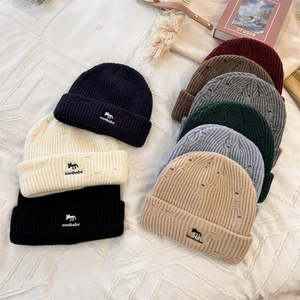Eight colors of distressed knit beanies with animal embroidery patch on a styled background