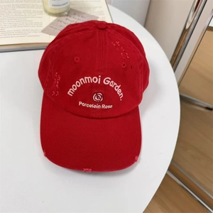 Distressed red cotton baseball cap with rose embroidery and wide brim on a white table