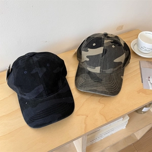 Outdoor camouflage baseball caps in green and black colors on a wooden table