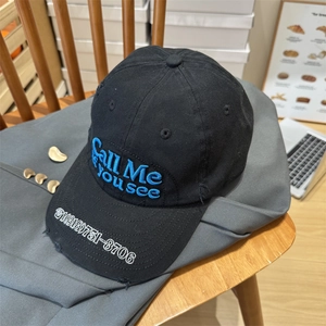 Distressed black cotton baseball cap with blue embroidery on a grey blazer and chair