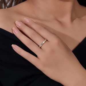 Close-up of a gold baguette-cut zircon eternity ring worn on a model against black knit fabric