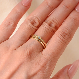 Nahaufnahme eines goldfarbenen Doppelring-Sets mit Zirkonia auf einem warmen Stoffhintergrund
