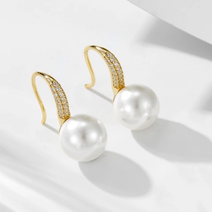 Close-up of white pearl drop earrings with gold micro-pave zircon hooks on white background