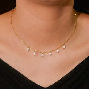 Elegant gold necklace featuring six small round white pearls worn on a woman's collarbone