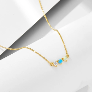 Detail of gold necklace featuring three circular opal and zircon stones on a white stone