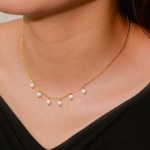 Close-up of minimalist gold choker necklace featuring six round white pearls on a model