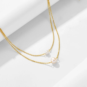 Détail d'un collier doré double rang avec deux perles blanches sur fond blanc minimaliste