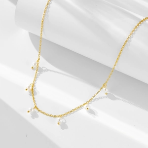 Detail of elegant gold chain necklace featuring multiple white pearls on a minimalist background