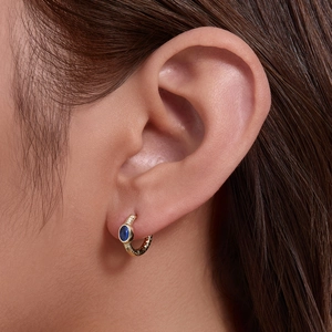 Textured gold hoop earring with oval blue gemstone worn by a fashion model