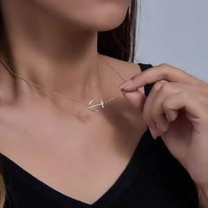 Detailed view of a gold anchor pendant necklace worn elegantly on a model's neck