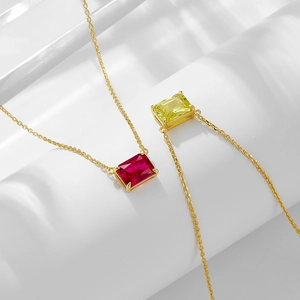 Minimalist gold necklace set with red and yellow rectangular zircon pendants on white stand