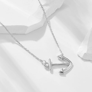 Minimalist silver anchor arrow pendant necklace displayed on a textured white stone